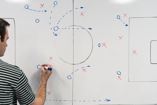 Entrenador de fútbol explicando las estrategias que se aplicaran durante el partido y/o el entrenamiento. Preparar las sesiones de entrenamiento o los partidos es otra de las siete funciones del entrenador de fútbol.